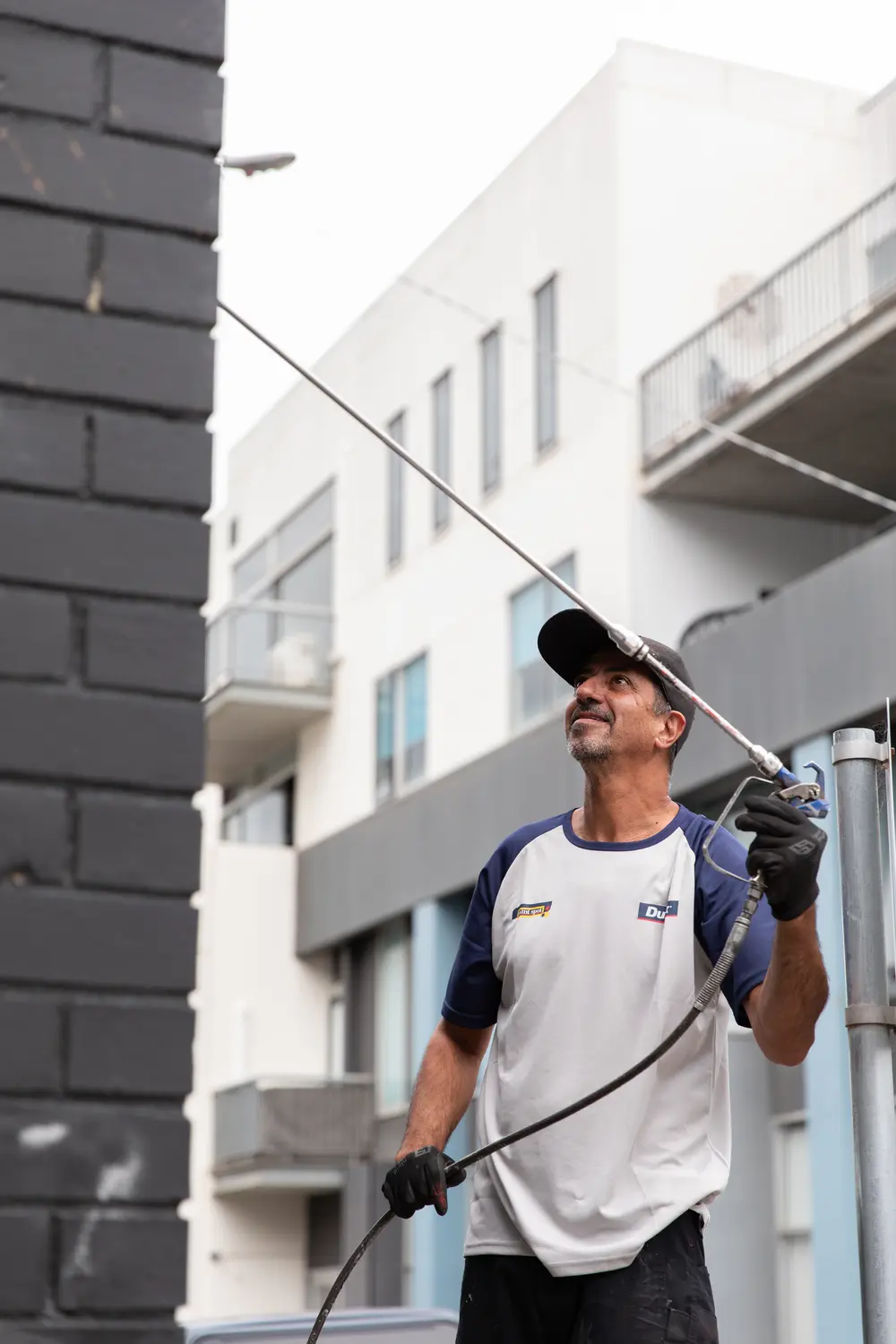 Rafael spray painting a building exterior from ground level
