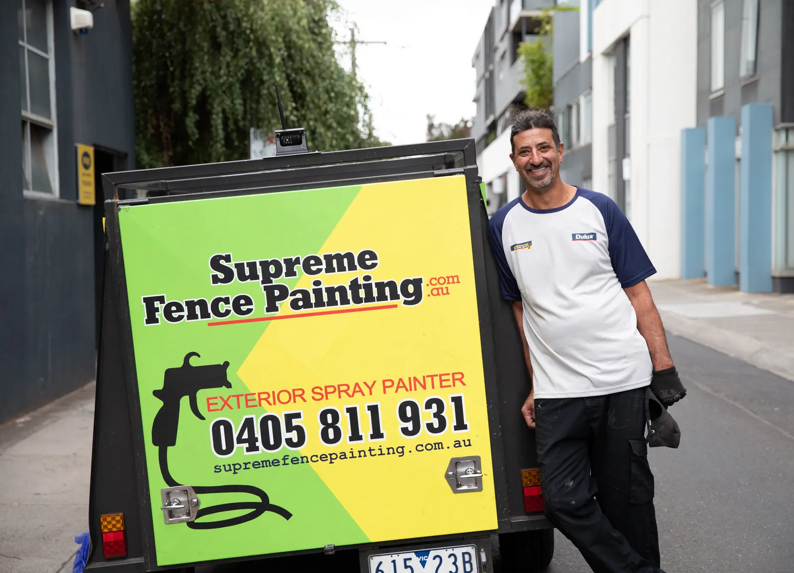Rafael smiling beside his Supreme Fence Painting trailer in a Melbourne street