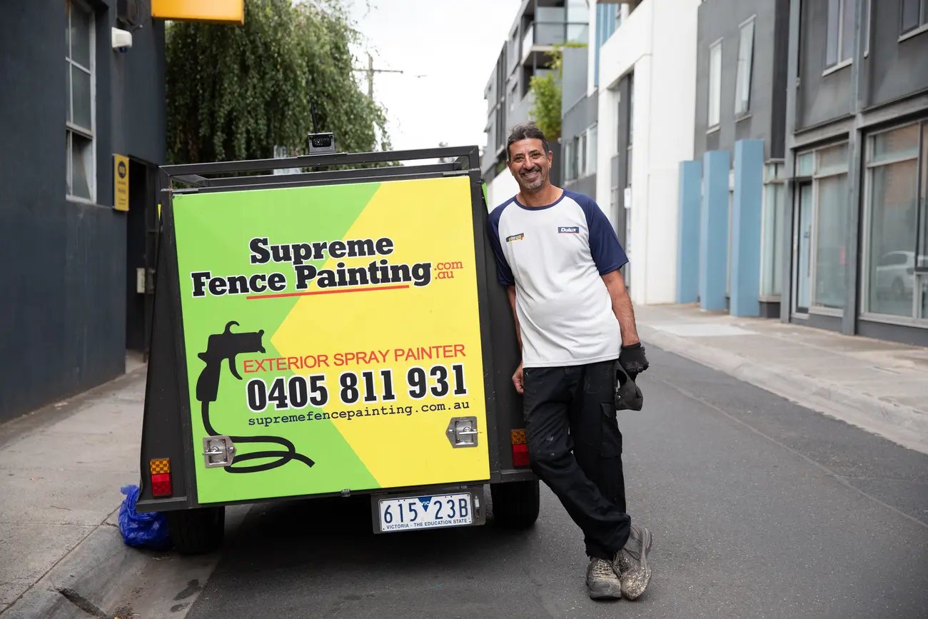 Rafael leaning on his yellow Supreme Fence Painting trailer, smiling